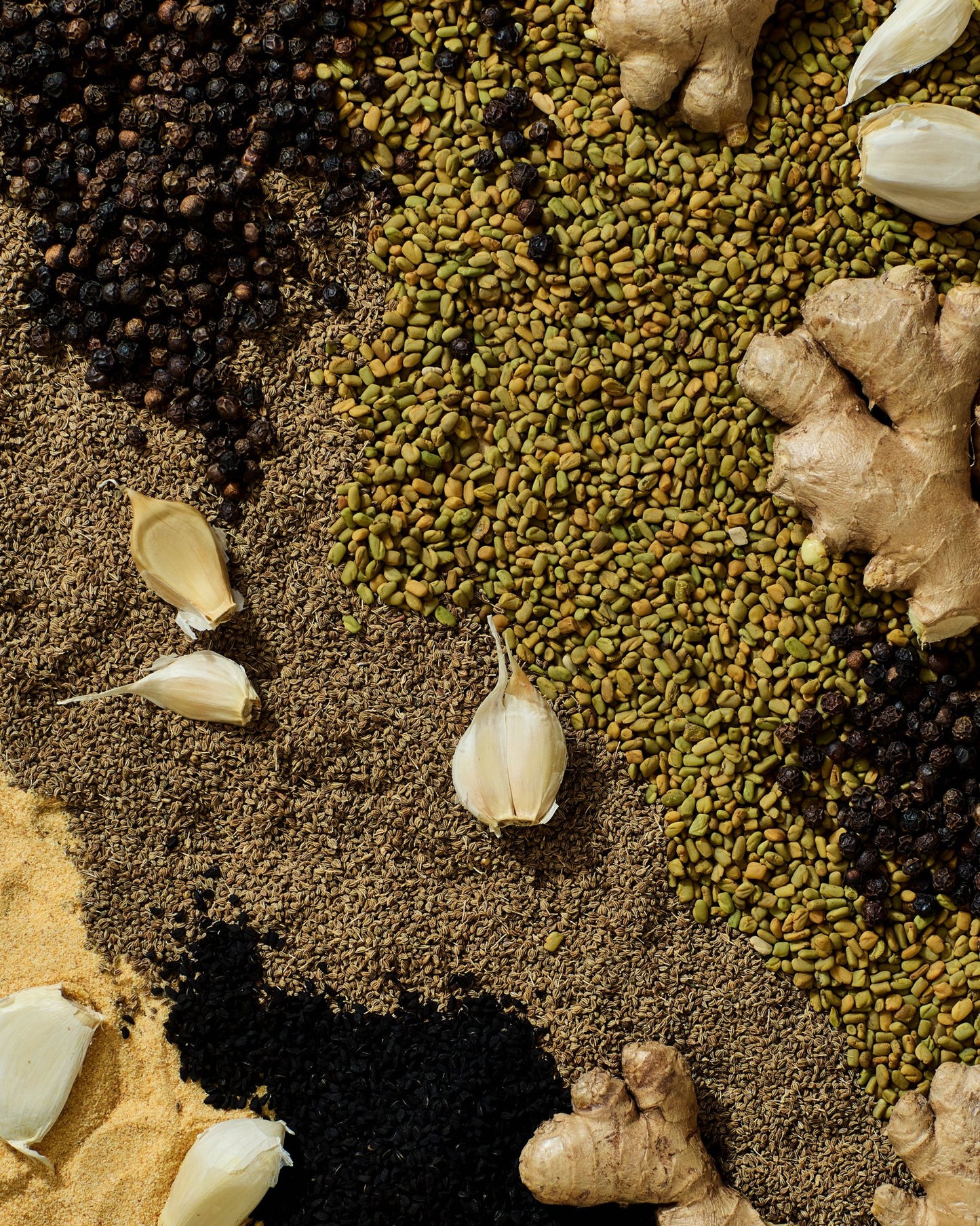 Flat lay of Makulaya spice mix ingredients including garlic, black seeds, ginger, ajwain, fenugreek, and black pepper.