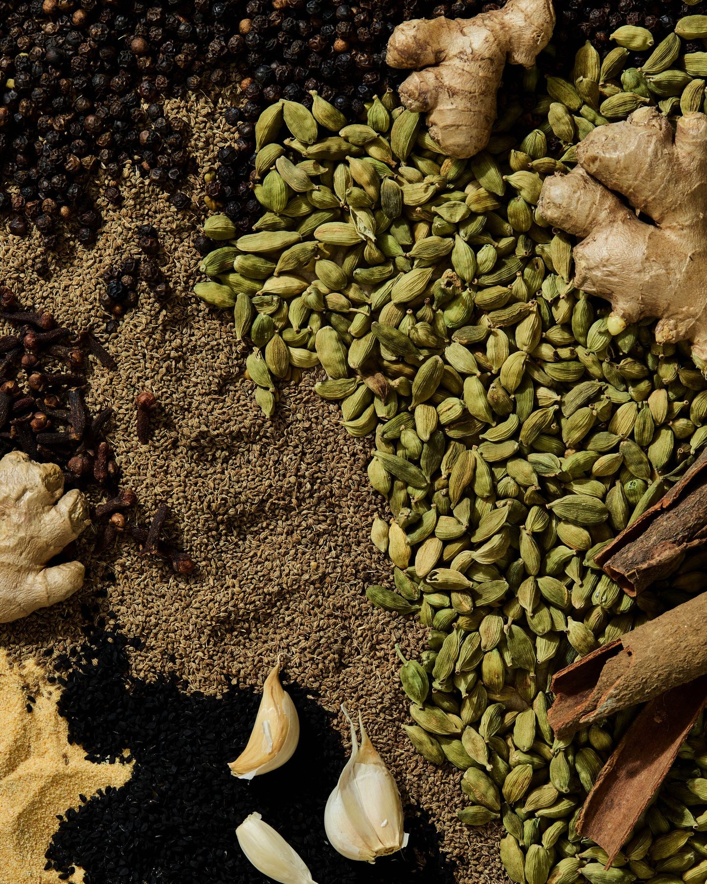 Flat lay of Ethiopian spices including green cardamom pods, cinnamon, ginger, ajwain, garlic, and black seeds used in Matafecha blend.