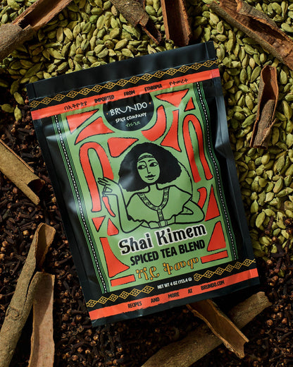 Brundo Spice Company Shai Kimem Spiced Tea Blend pouch on a bed of green cardamom, cinnamon bark, and cloves.
