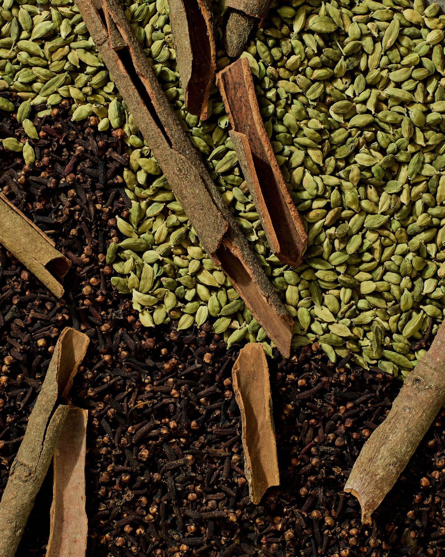 Flat lay of traditional Ethiopian tea spices including green cardamom pods, cloves, and cinnamon bark used in Shai Kimem blend.