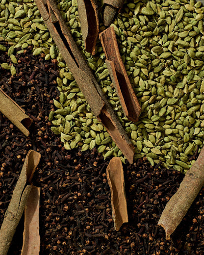 Flat lay of traditional Ethiopian tea spices including green cardamom pods, cloves, and cinnamon bark used in Shai Kimem blend.